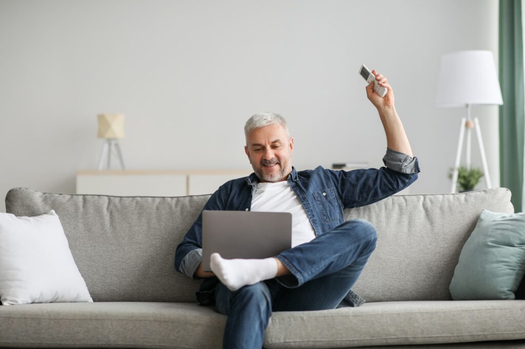 Relaxed man sitting on couch with laptop, turn on AC